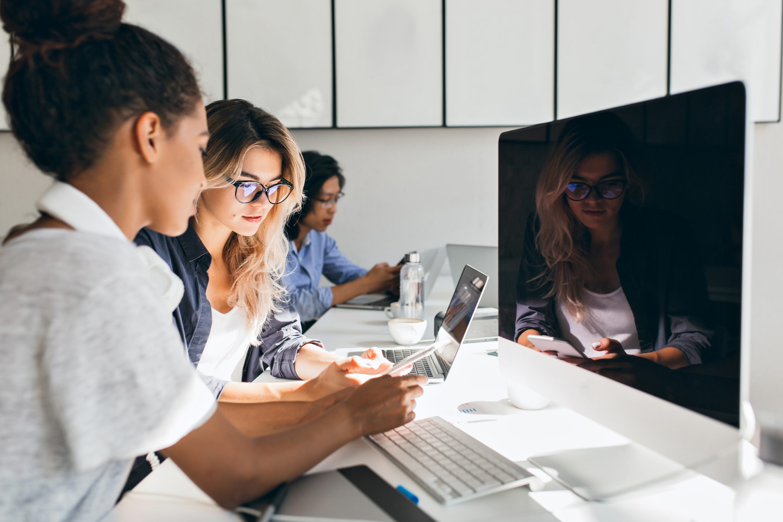 black female it specialist sitting beside modern computer with black screen talking with friends indoor portrait busy young people working international company scaled